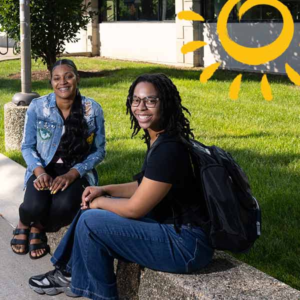 three students sitting at a table outside on campus with an overlay of a sun graphic