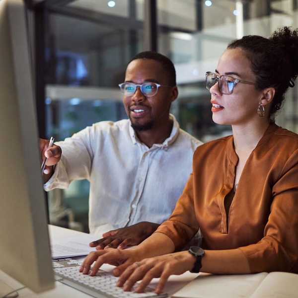 Man and woman sitting in front of computer screen and the woman is typing on the computer keyboard.
