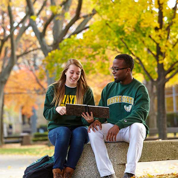 A male and female students sitting outside on campus during fall season