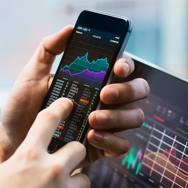 A hand holding a phone with stock price charts on it market