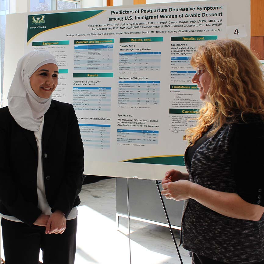 Two women, one wearing a hijab, presenting a research poster.