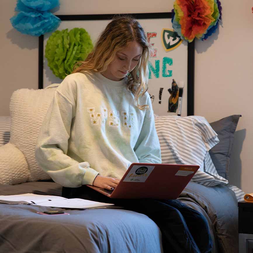 Woman sits on a dorm room bed studying