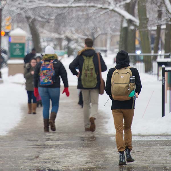 the backs of students walking down a sidewalk on campus in the snow