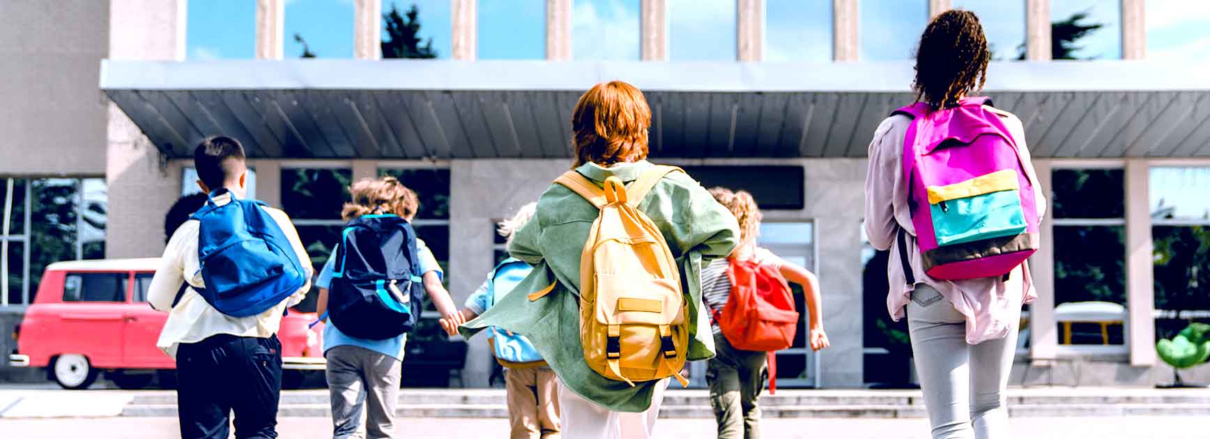 Children with backpacks running toward a school